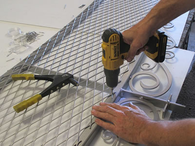 A man is fixing expanded metal mesh onto a frame door top.