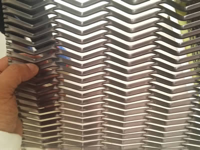 On hand is holding one piece of raised expanded metal with folded design, forming wave patterns.